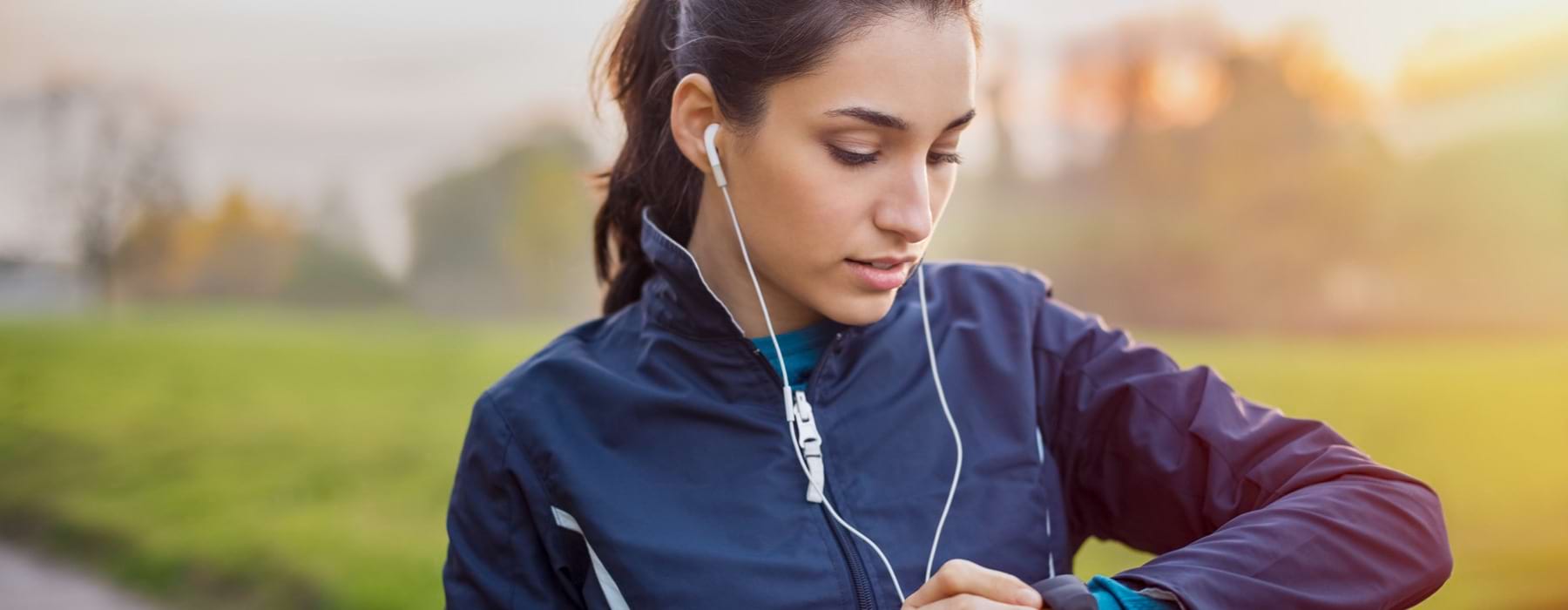 young woman with earbuds in her ears, on a run, stops to look at her watch